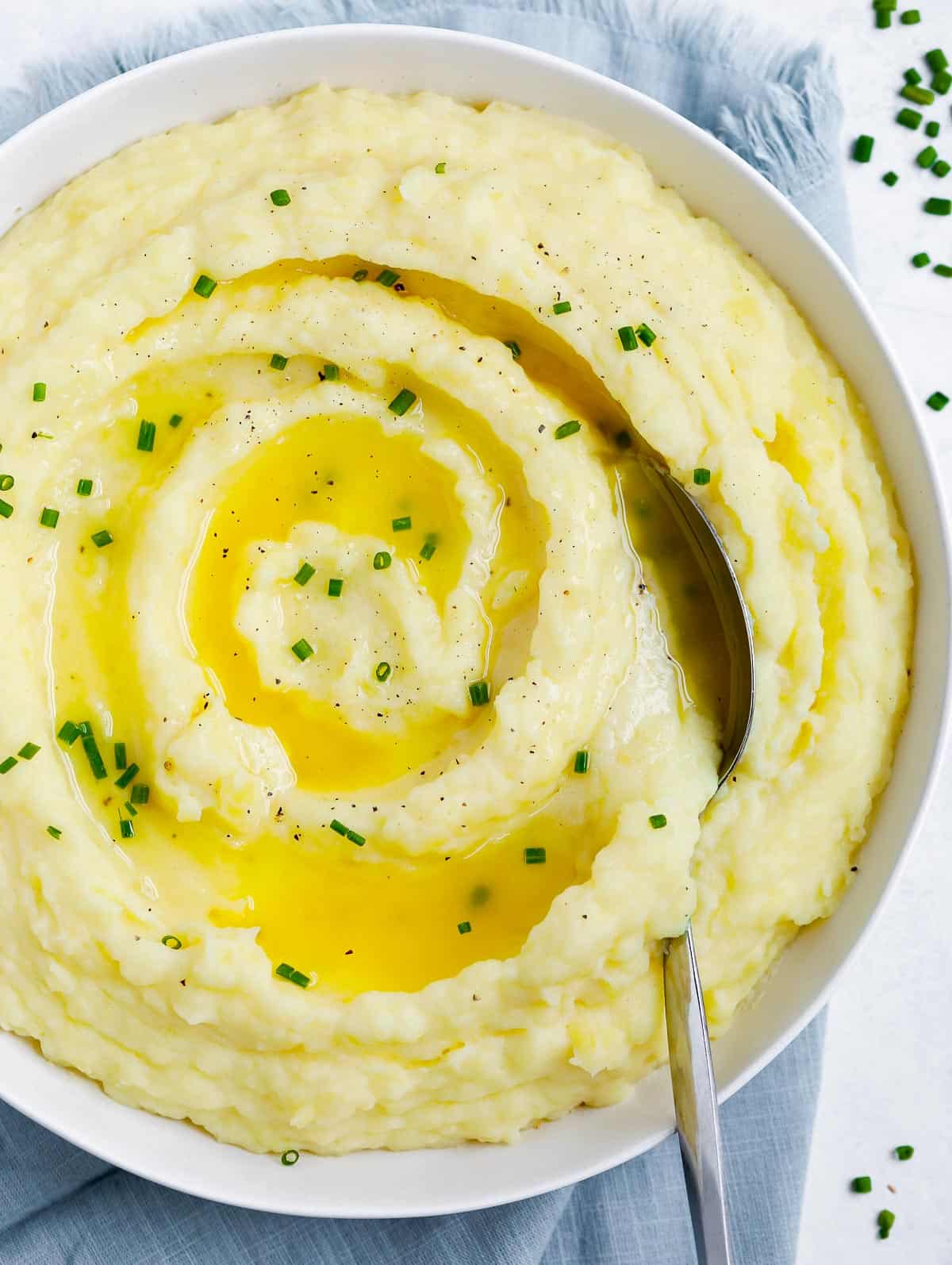 creamy mashed potatoes in a white plate topped with melted butter and chives, with a spoon in the plate