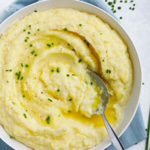 creamy mashed potatoes in a white plate topped with melted butter and chives, with a spoon in the plate