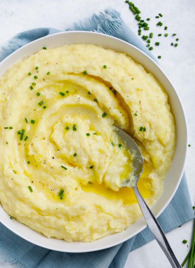 creamy mashed potatoes in a white plate topped with melted butter and chives, with a spoon in the plate