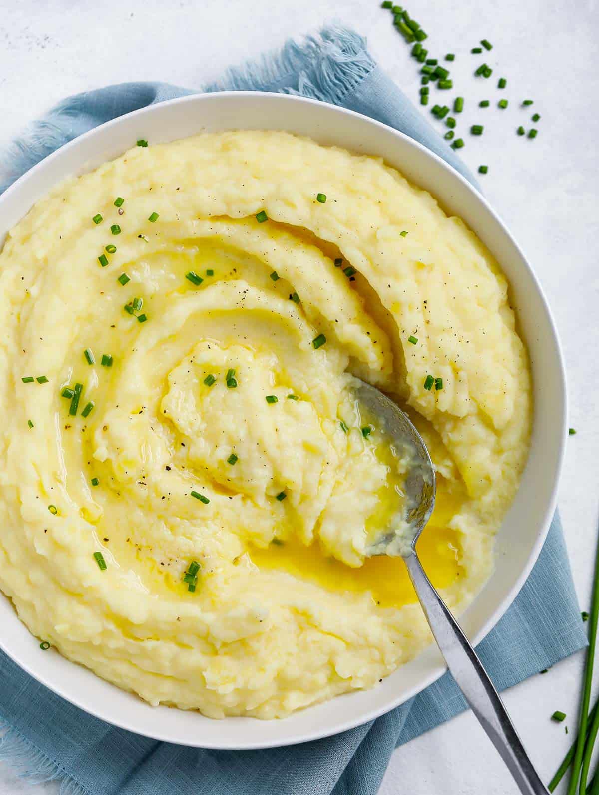 creamy mashed potatoes in a white plate topped with melted butter and chives, with a spoon in the plate