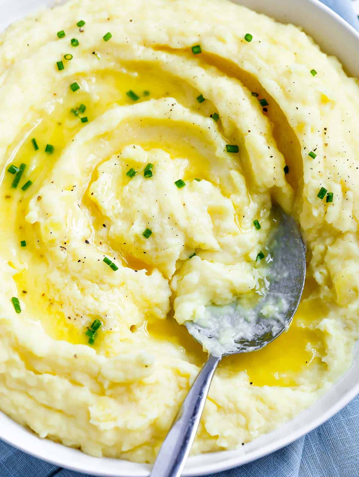 creamy mashed potatoes in a white plate topped with melted butter and chives, with a spoon in the plate