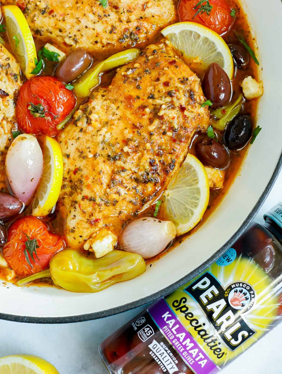 Close up of baked greek chicken beside a jar of olives.