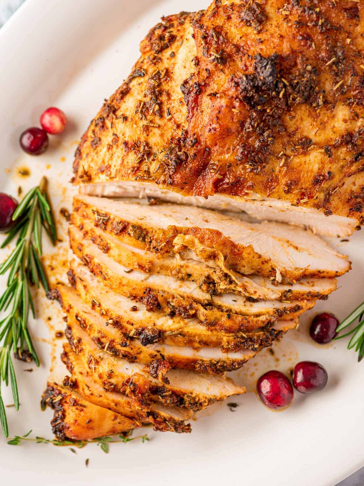 overhead shot of the roasted turkey breast halfway sliced on a white plate with cranberry and rosemary stalks
