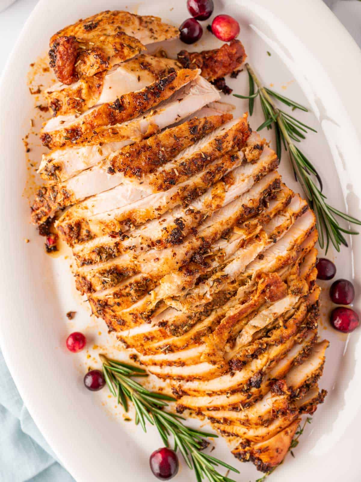 overhead shot of sliced turkey breast on a white plate with cranberry and rosemary stalks