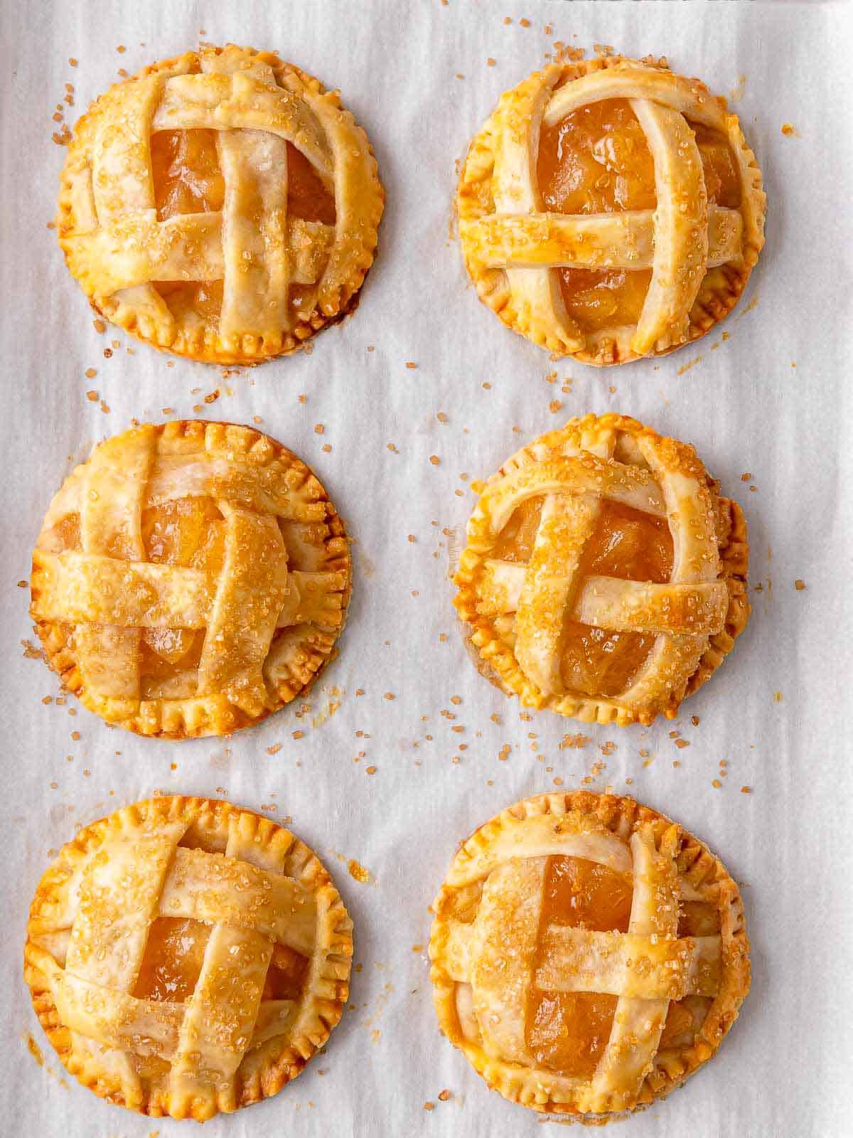 Individual apple pies with golden lattice tops on parchment paper.