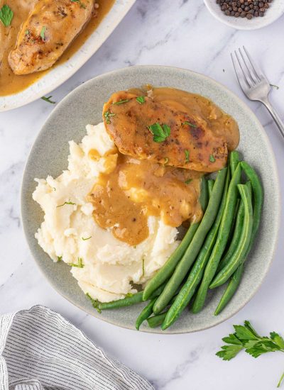 A plate of chicken, gravy, mashed potatoes, and green beans.