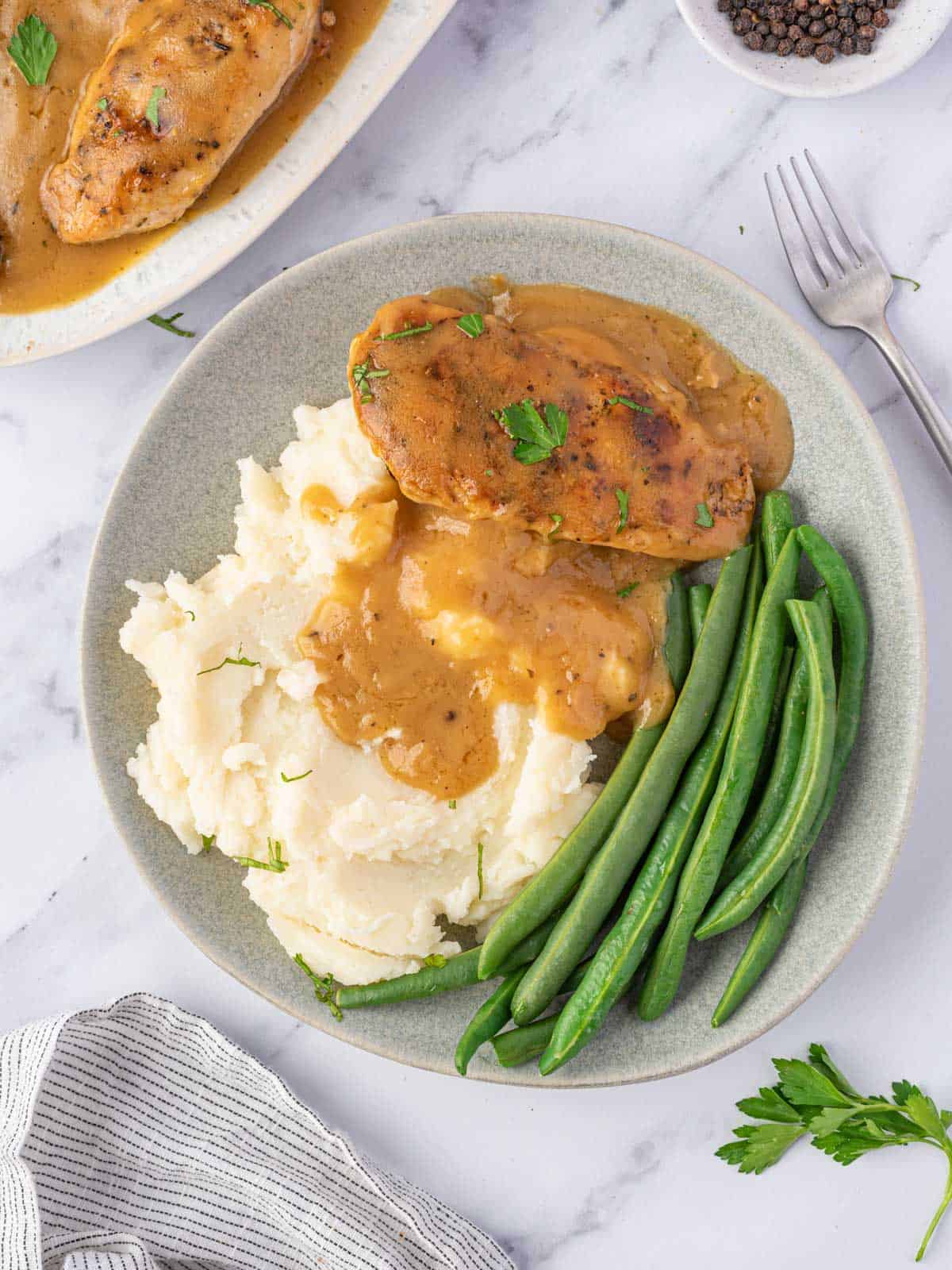 A plate of chicken, gravy, mashed potatoes, and green beans.