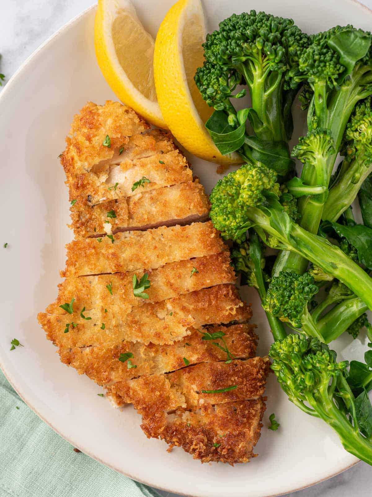 A plate of crispy parmesan chicken by broccoli.