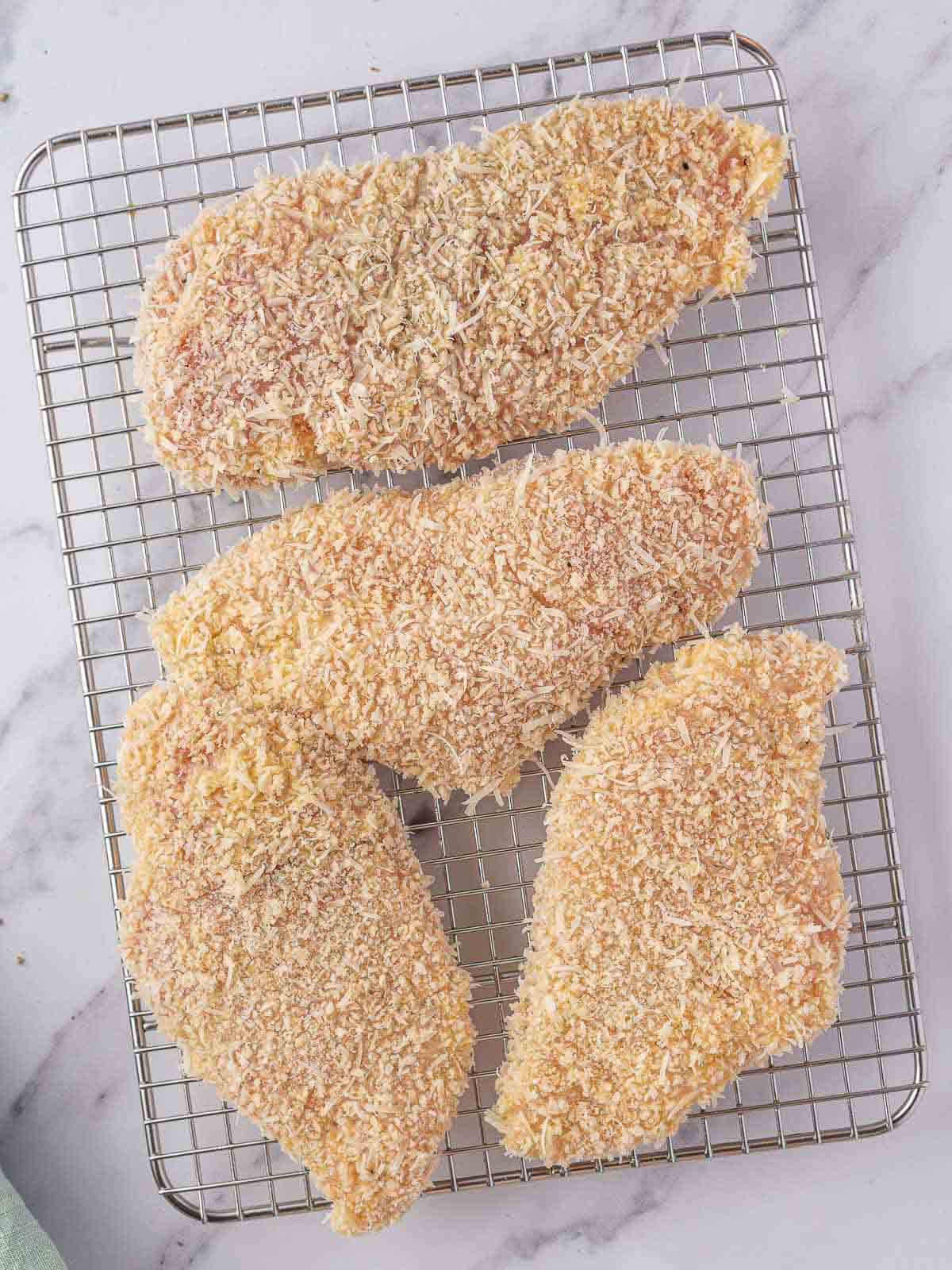 Coated chicken breasts on a wire rack.