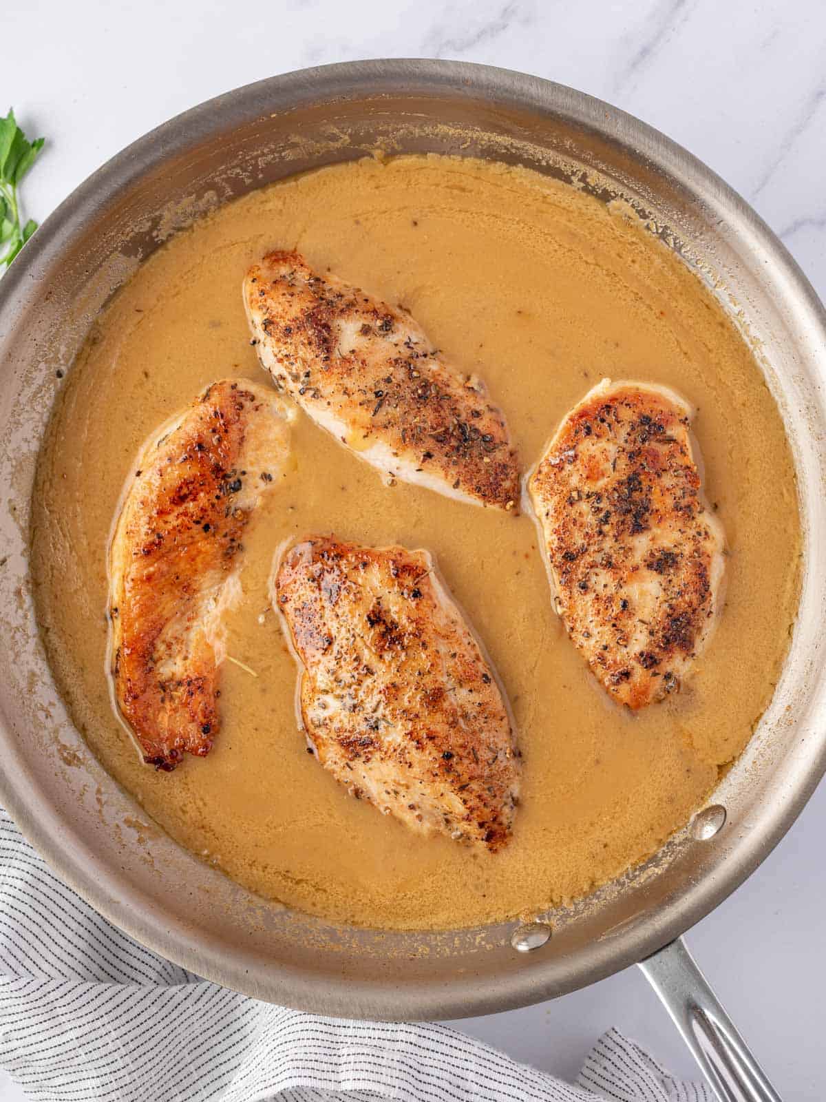 Seared chicken breasts simmering in homemade gravy.
