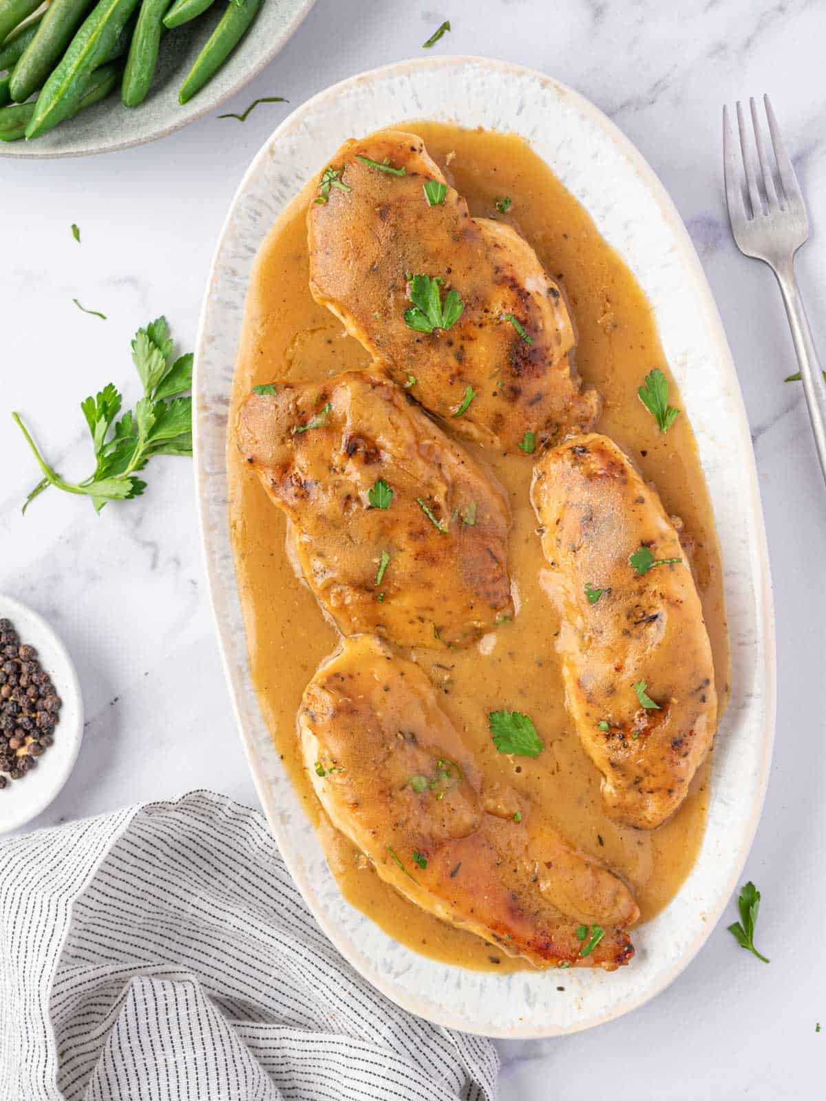 Chicken breasts covered with gravy and garnished with chopped parsley.