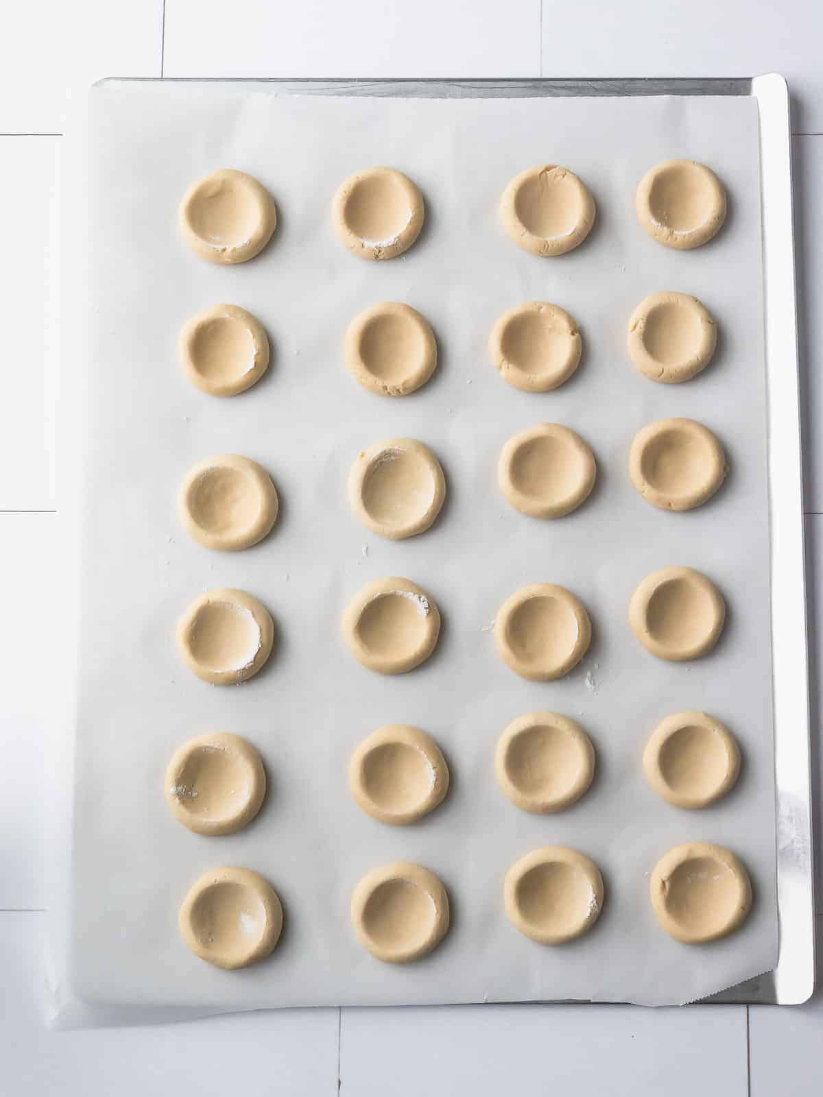 Cookie dough balls with center indents spaced across a parchment-lined baking sheet.