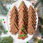 Rows of spiced tree cookies with M&M decorations arranged on a holiday platter.