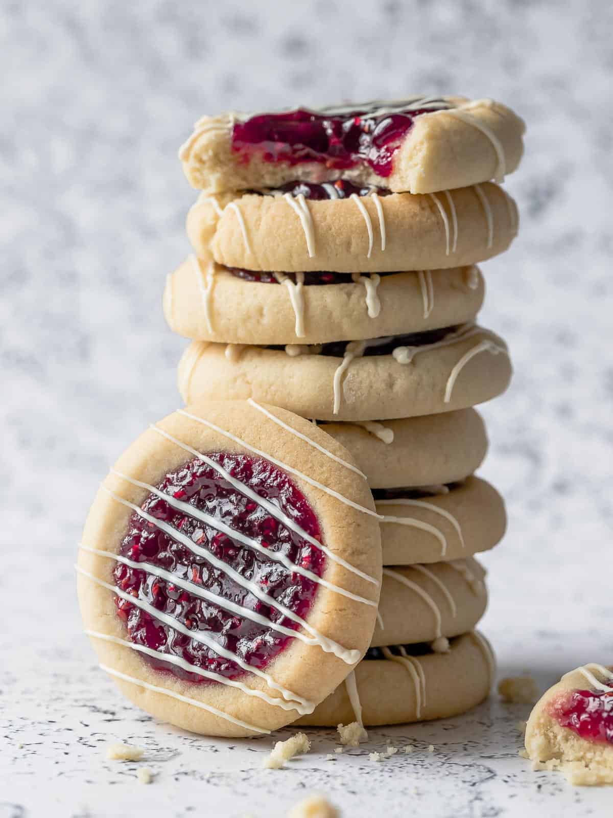 Jam Thumbprint Cookies stacked with raspberry jam centers and white chocolate drizzle.