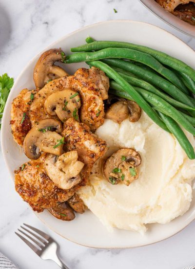 A plate of mushroom garlic chicken thighs with mashed potatoes and green beans.