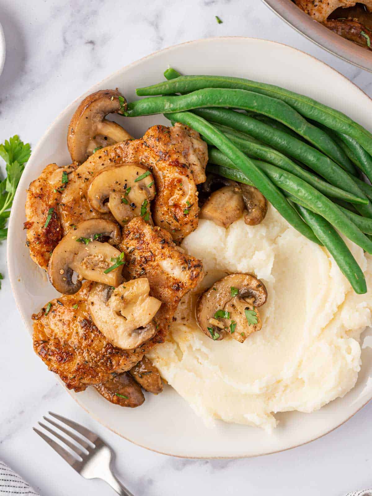 A plate of mushroom garlic chicken thighs with mashed potatoes and green beans.