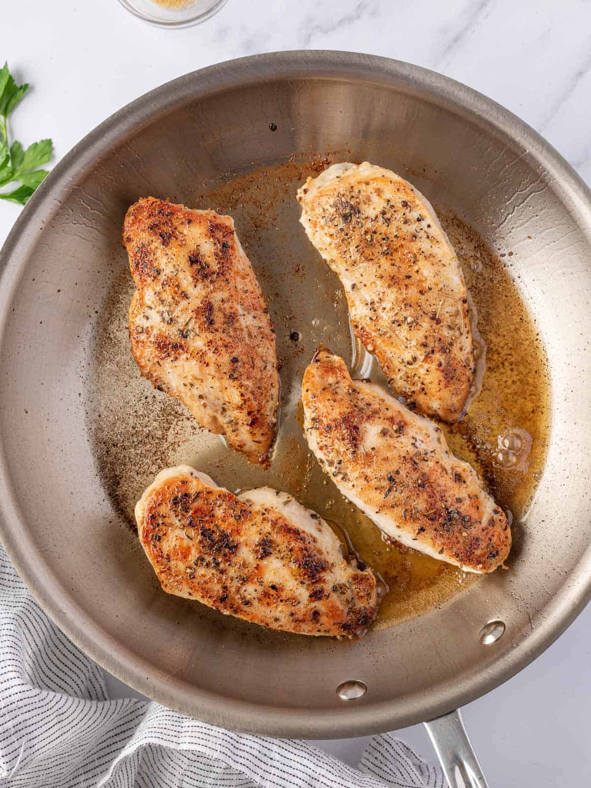 Seasoned chicken breasts seared until golden in a skillet.