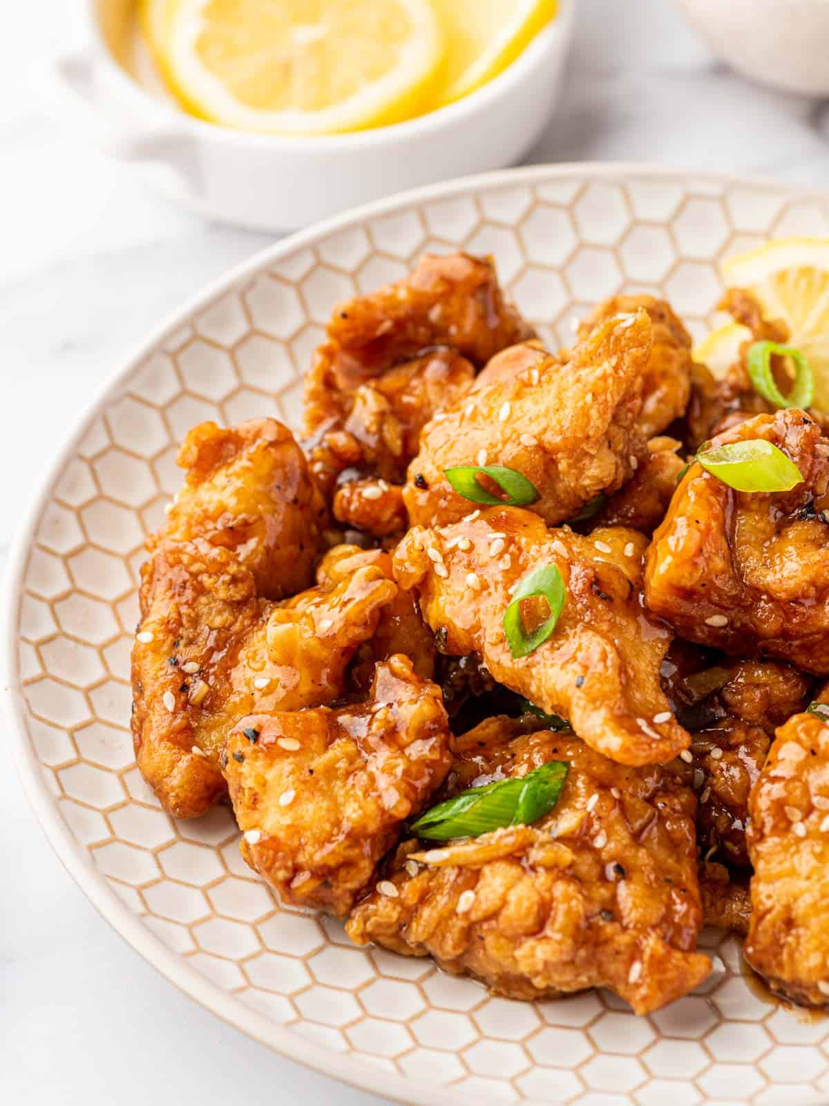 Chicken in lemon sauce topped with sesame seeds and sliced green onions on a white plate.