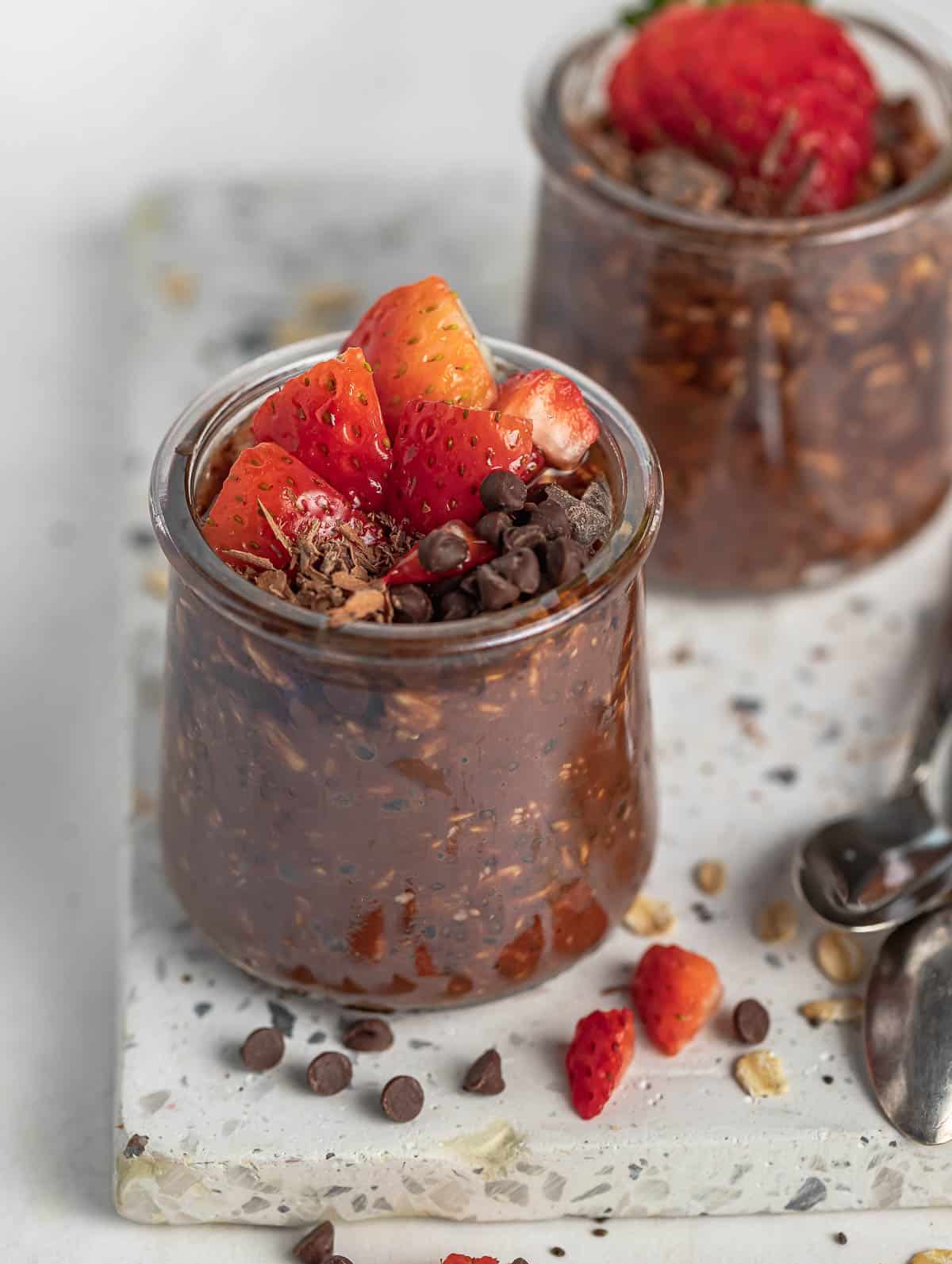 two cups of chocolate overnight oats topped with strawberry and chocolate chips