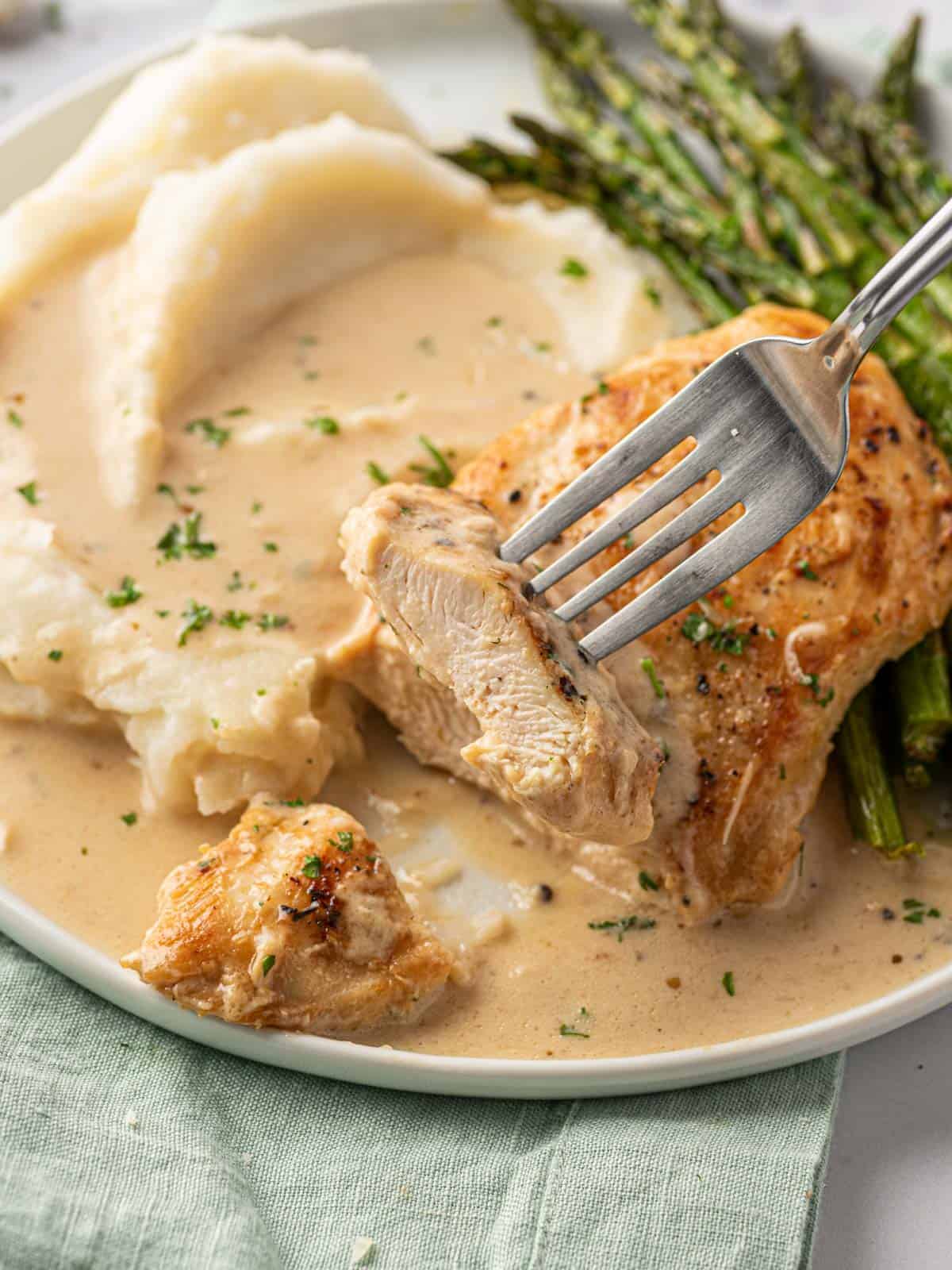 A piece of chicken lifted of a plate of creamy parmesan chicken.