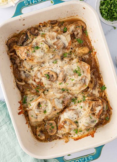 Overhead view of cheesy baked chicken breasts with mushrooms in a blue baking dish.