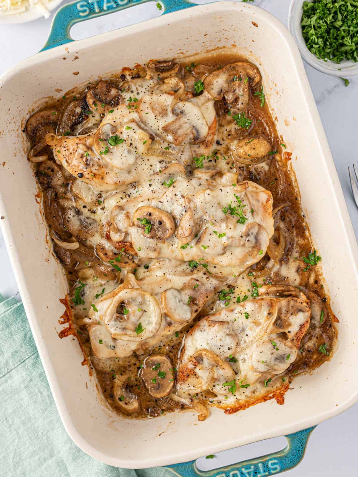 Overhead view of cheesy baked chicken breasts with mushrooms in a blue baking dish.