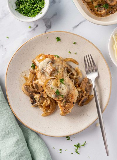 Overhead view of a plate of cheesy baked chicken breasts with mushrooms with a fork on the plate.