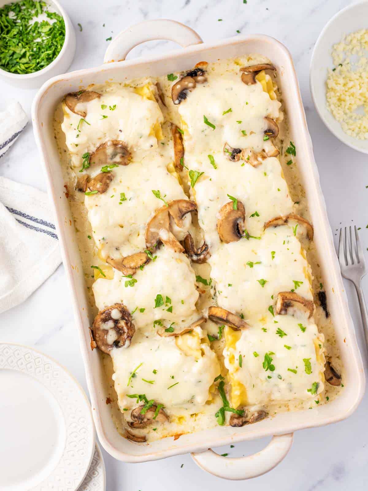 8 chicken alfredo lasagna rolls in a casserole dish with melted cheese on top.
