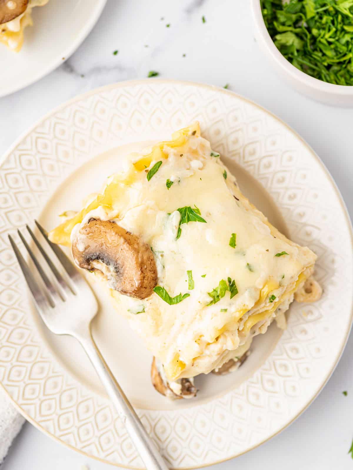 A white plate with a single serving of chicken alfredo lasagna rolls and a fork.