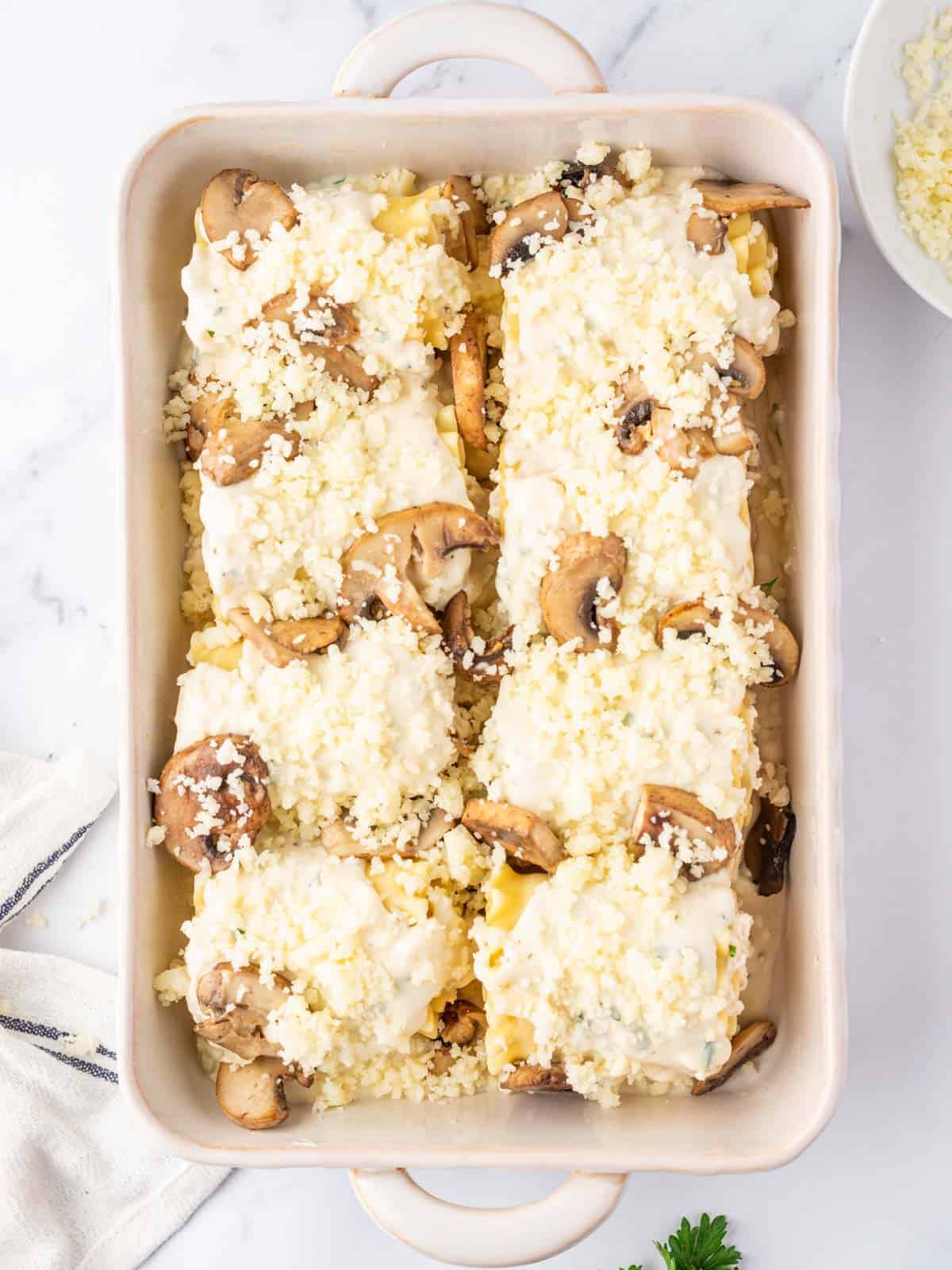 Casserole dish of 8 chicken alfredo lasagna roll ups with cheese sprinkled on top ready to bake.