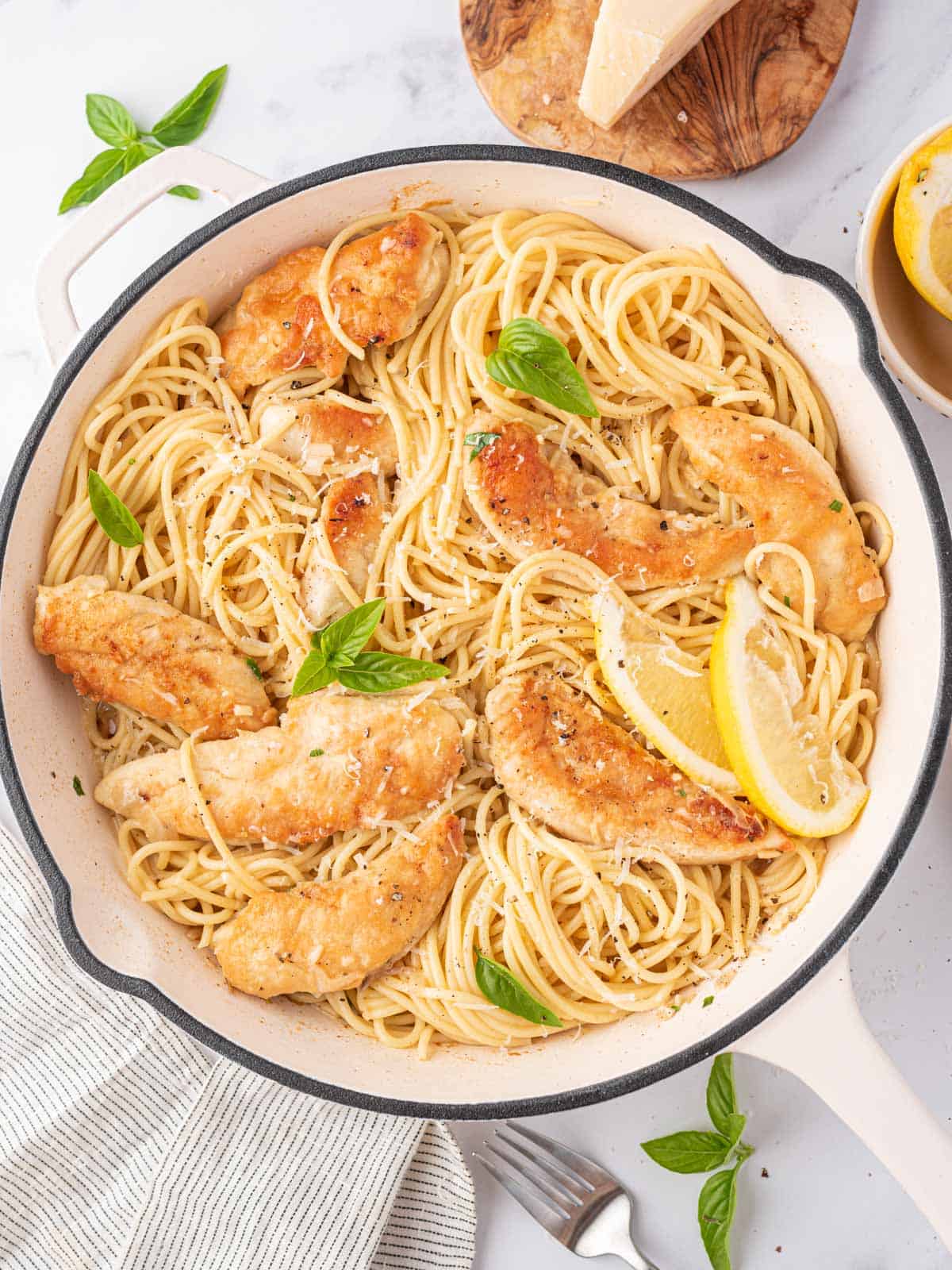 Chicken scampi with pasta in a bowl with a block of fresh parmesan in the background.