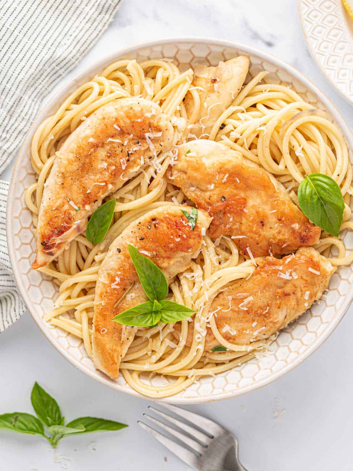 Chicken scampi in a bowl with pasta and topped with fresh basil.