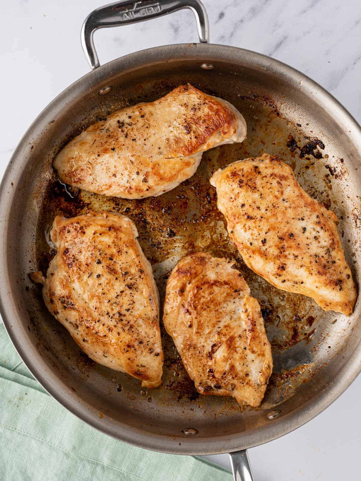 A pan with four cooked chicken breasts.