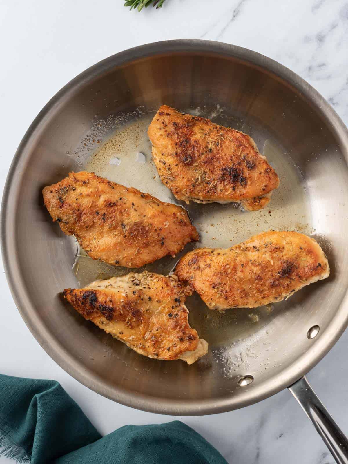 Chicken breasts seared in a pan.
