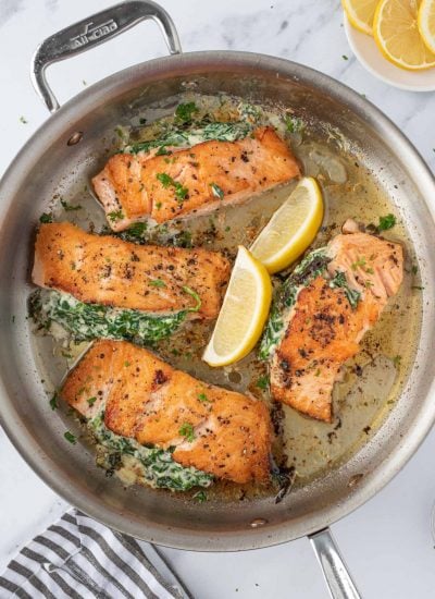 Overhead view of a pan of creamy stuffed spinach salmon with lemon wedges.