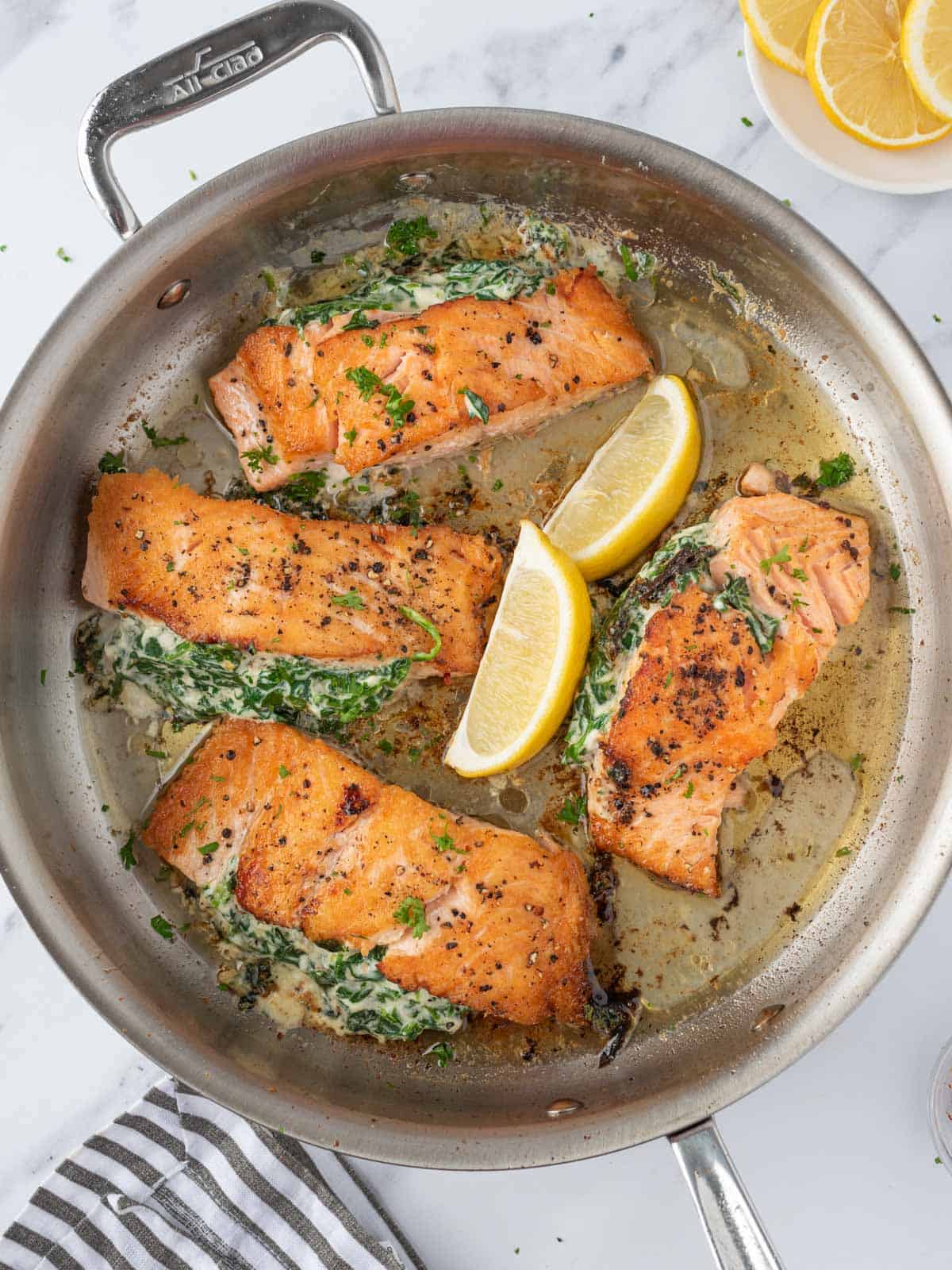 Overhead view of a pan of creamy stuffed spinach salmon with lemon wedges. 