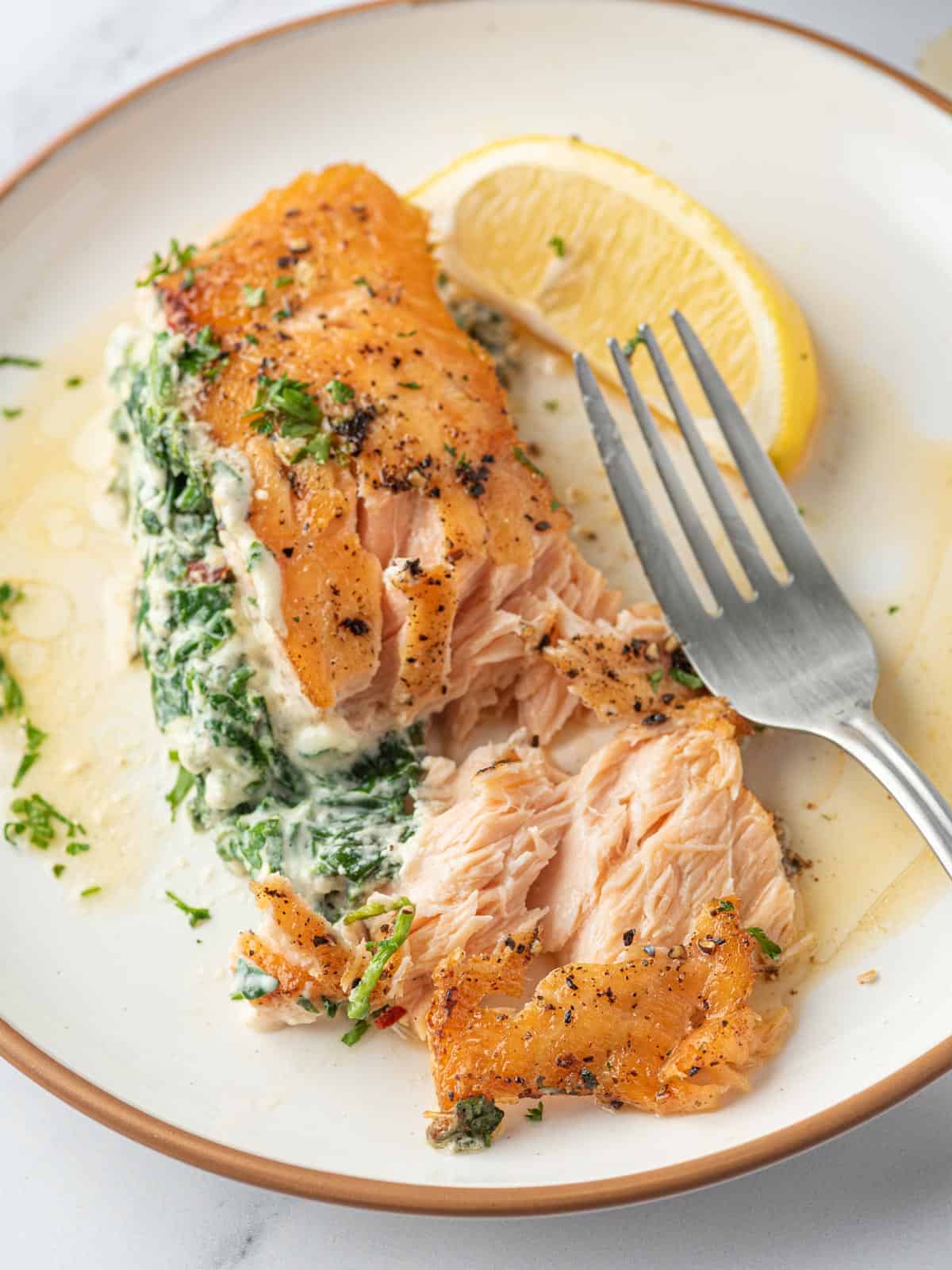 A plate of creamy stuffed spinach salmon with a part flaked opened.