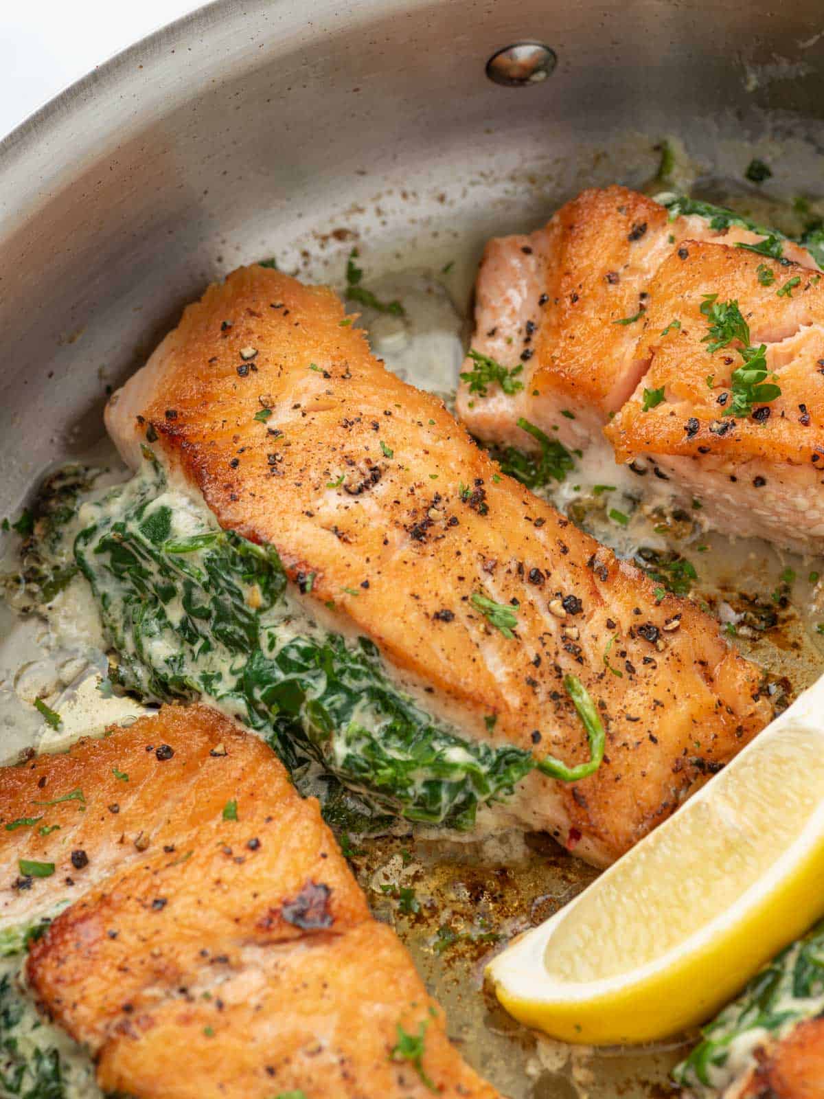 A pan of creamy stuffed spinach salmon with a lemon wedge.