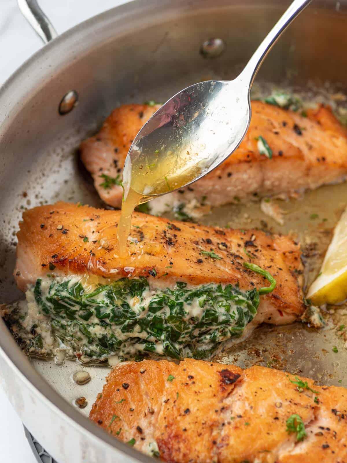 A pan of creamy stuffed spinach salmon with sauce spooned on top.