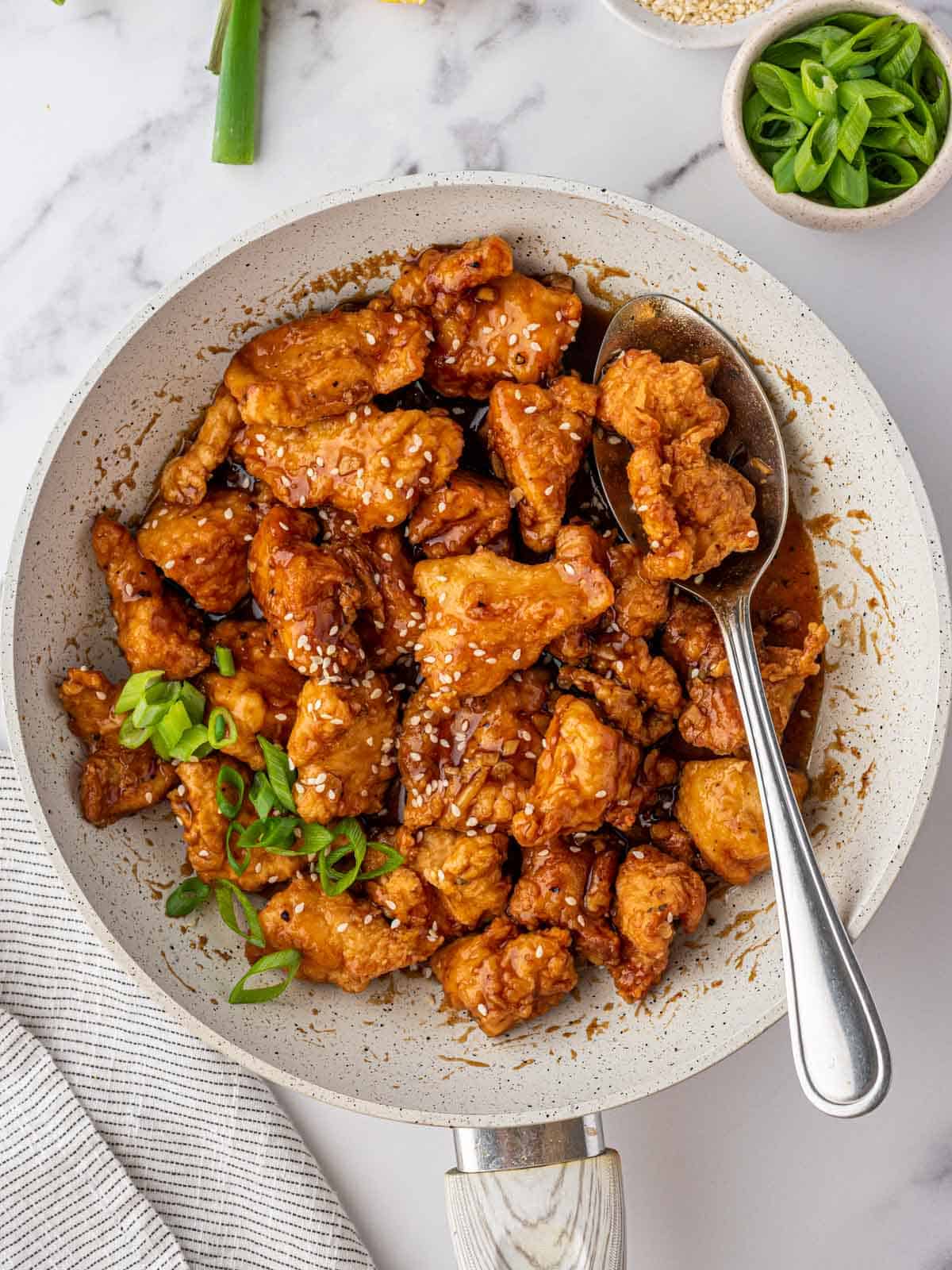 A large bowl of Asian lemon chicken with a serving spoon.