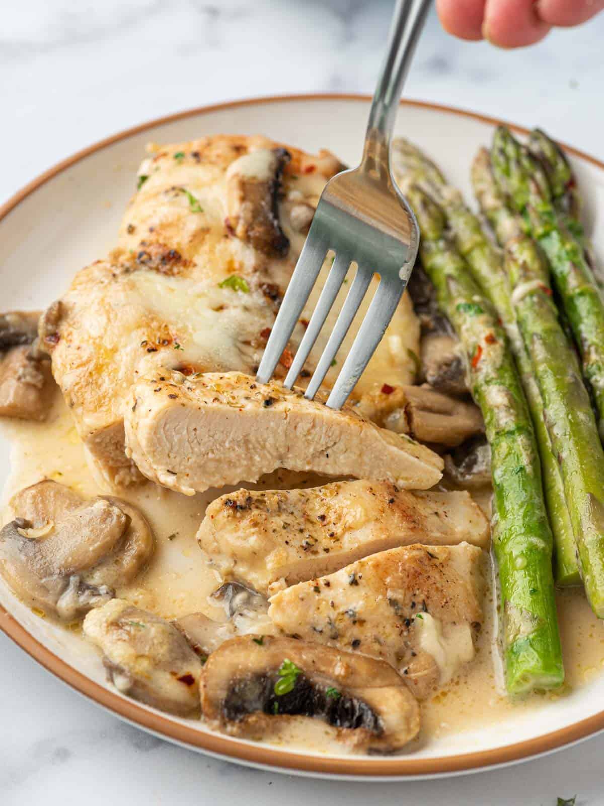 A plate with chicken madeira, mushrooms, and asparagus.