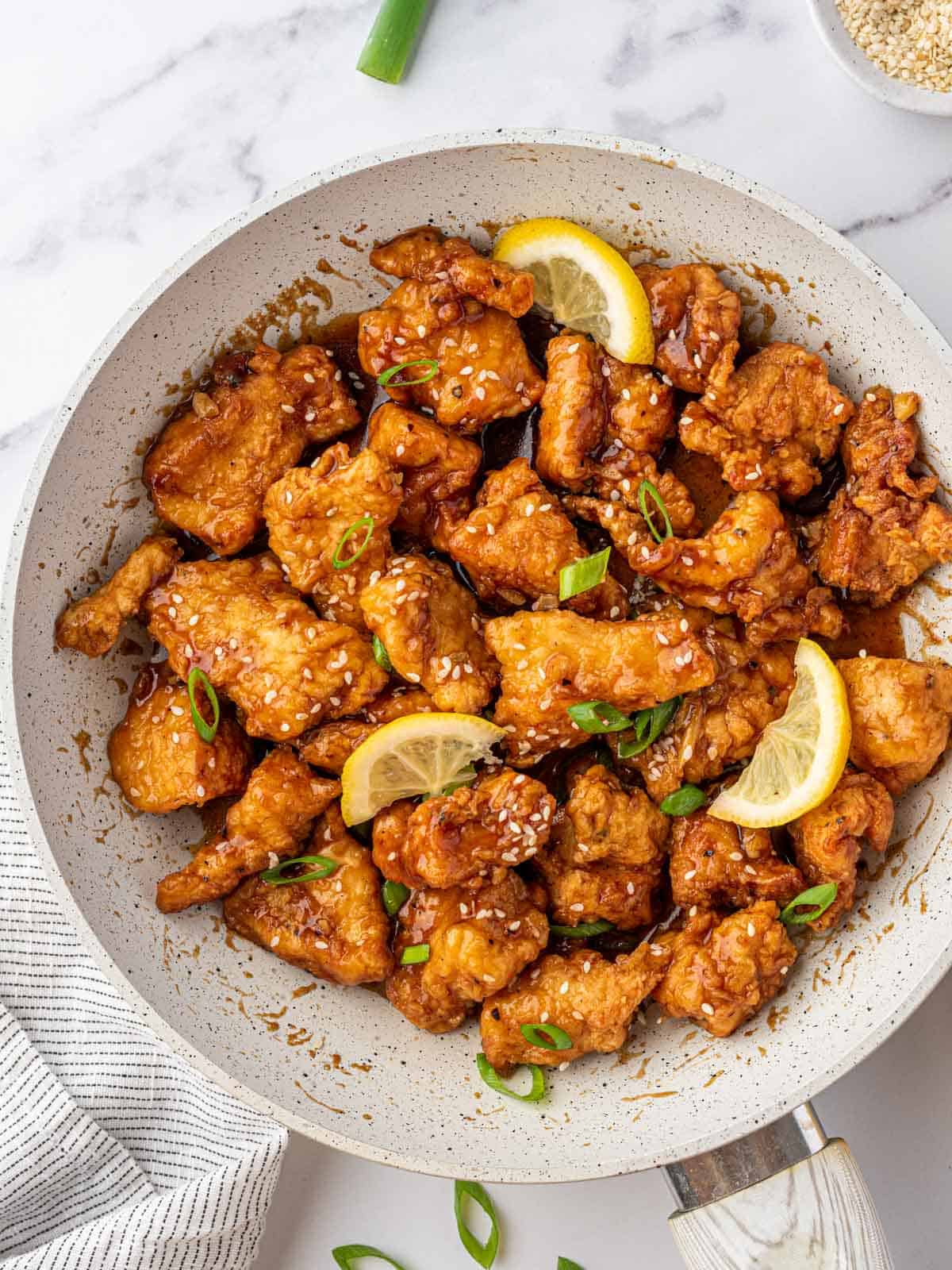 Skillet full of lemon chicken topped with green onions, sesame seeds and three fresh lemon wedges.