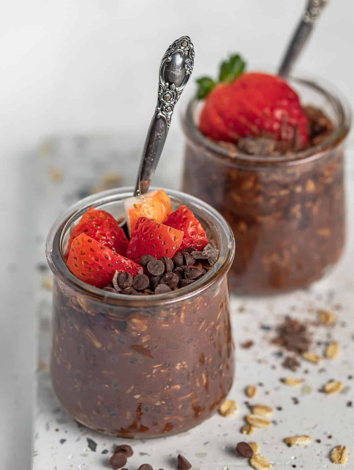 two cups of chocolate overnight oats topped with strawberry and chocolate chips