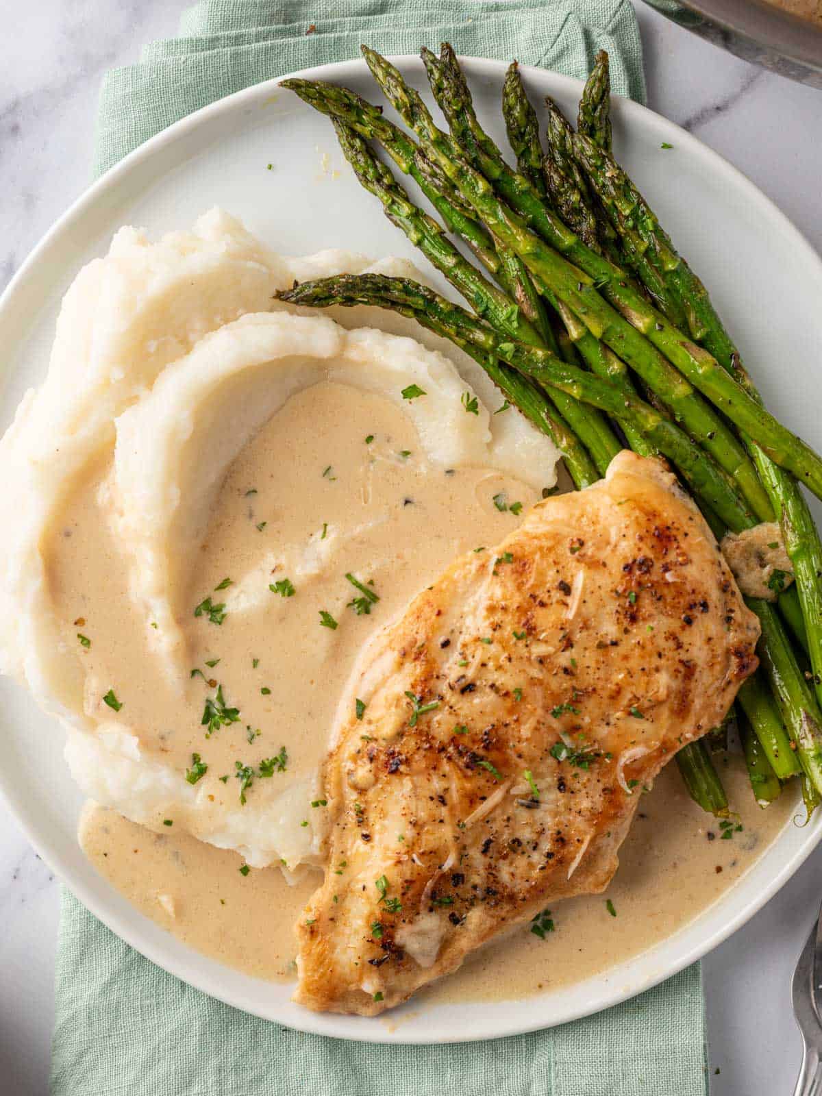 A plate of creamy garlic parmesan chicken with mashed potatoes and asparagus.