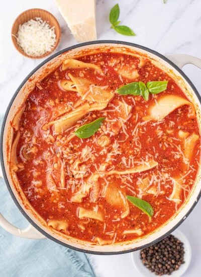 A top view of one pot lasagna soup with a few leaves of green basil and a small bowl of parmesan cheese to the side.