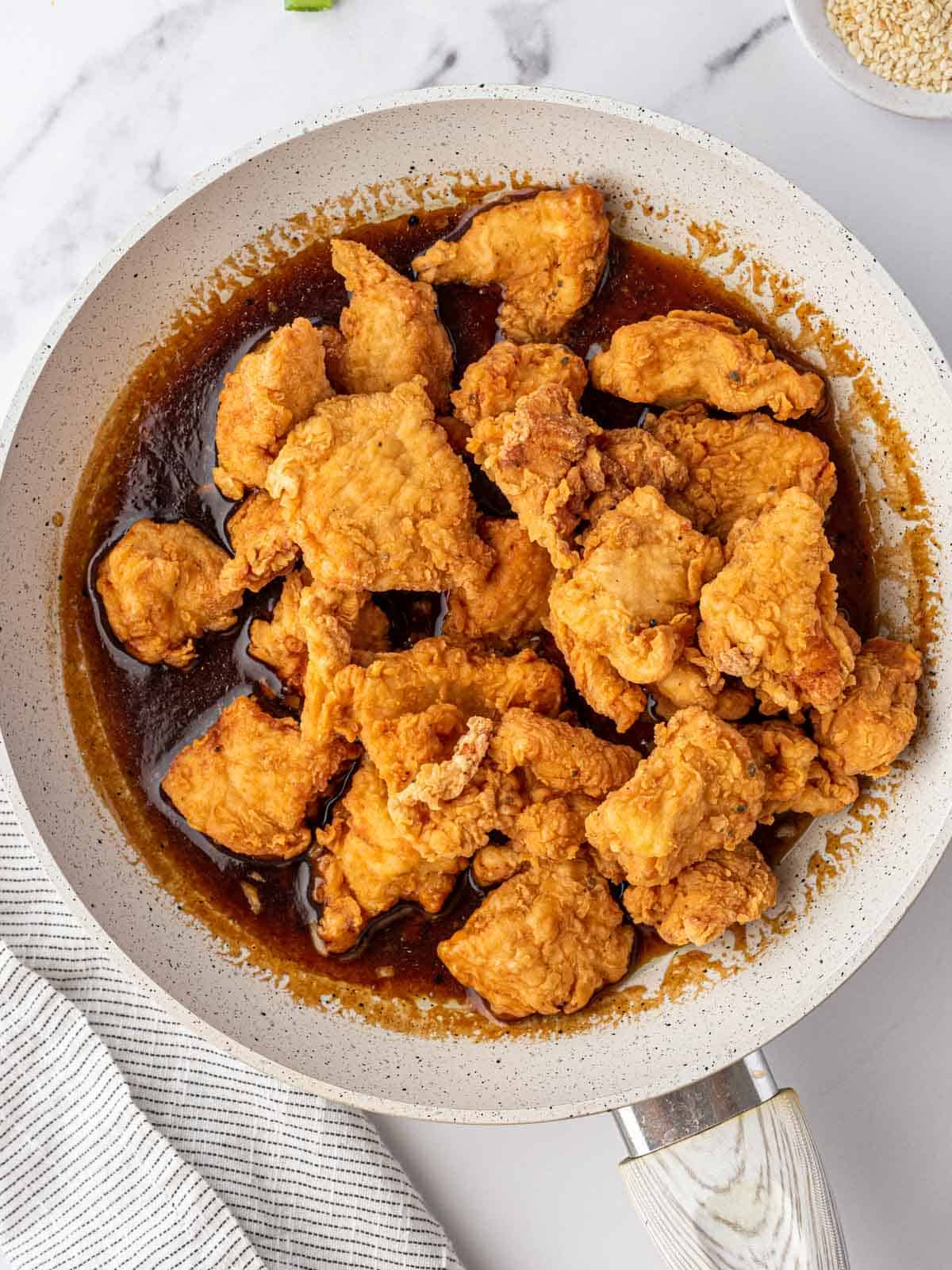 Crispy fried chicken in skillet of Chinese lemon sauce.