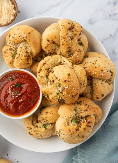 A plate of garlic knots with a small bowl of sauce.