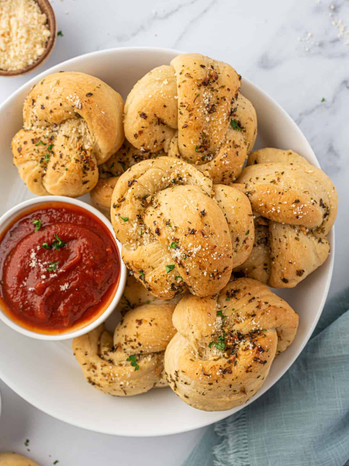 A plate of garlic knots with a small bowl of sauce.