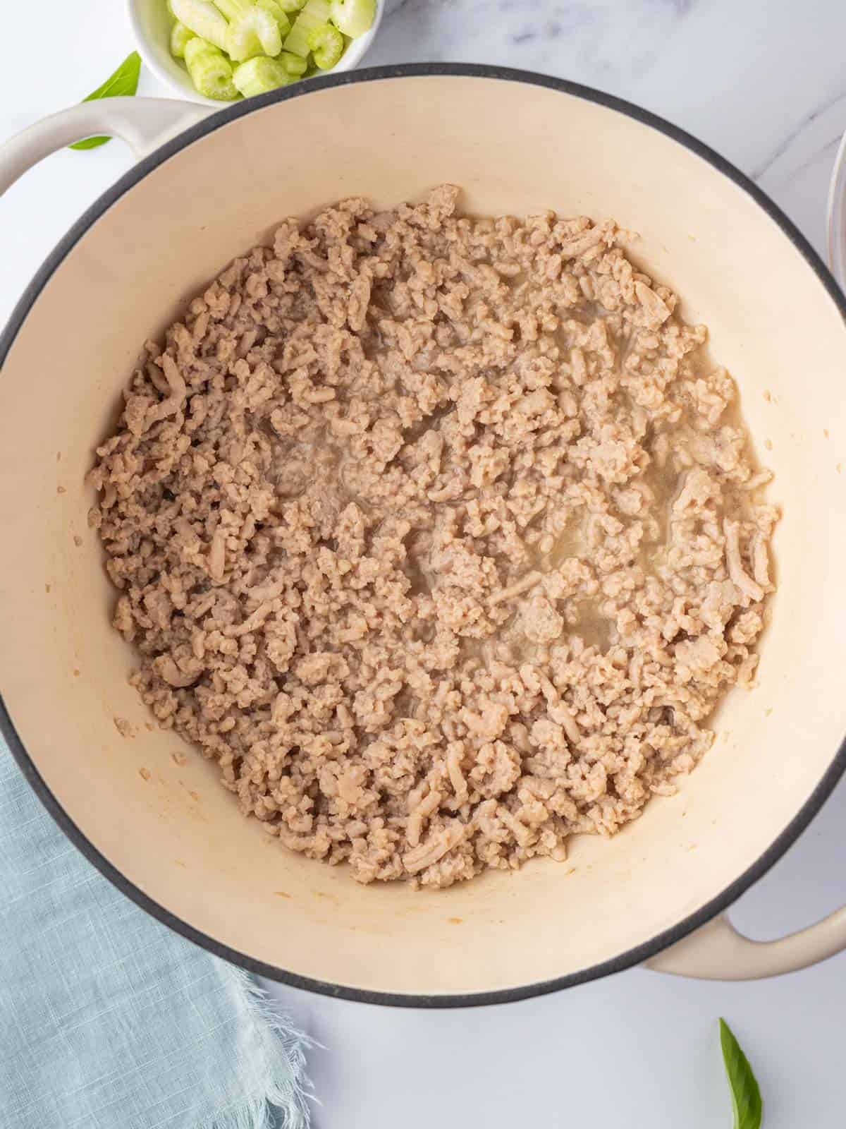 Browning ground chicken in a white dutch oven.