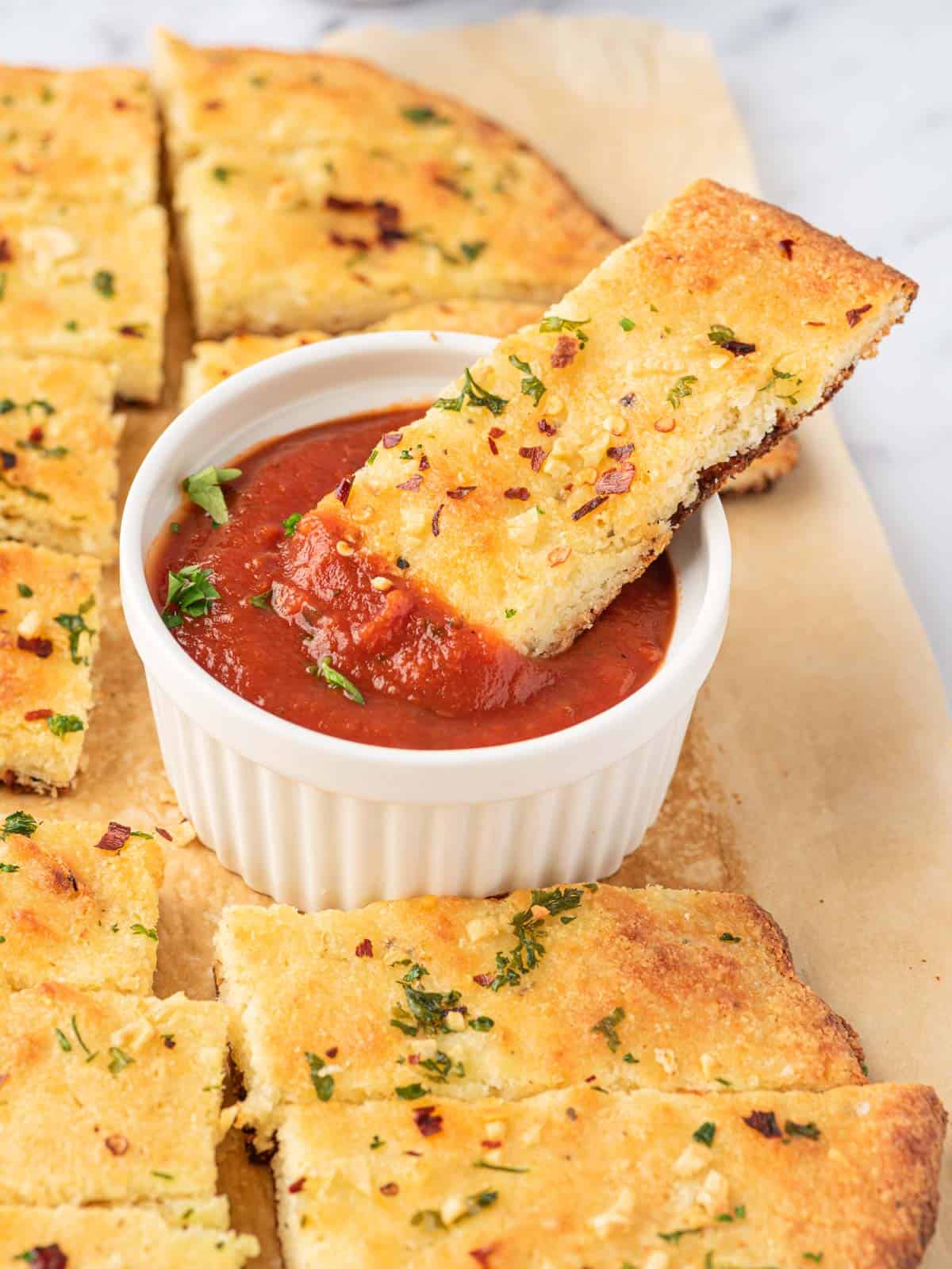 A piece of low carb garlic bread dipped into a bowl of marinara sauce.